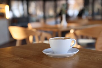 Fototapeta premium Cup of aromatic coffee on wooden table in cafe, closeup. Space for text
