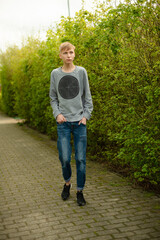 Fototapeta premium Smiling Blond Man in Blue Jeans and Gray Sweater Walking in Park Happy and Relaxed