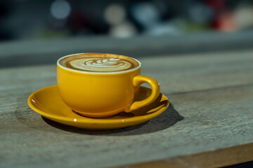 A yellow cup of hazelnut latte placed on a wooden table, photographed at night with an eye level angle