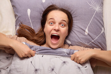 A woman with long hair sits up in bed, her arms pulling back the covers. She expresses excitement...