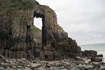 Towering cliffs with a natural arch silhouette against an overcast sky. Rugged gray rocks and...