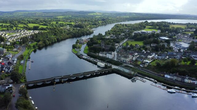 Killaloe, County Clare, Ireland, September 2021. Drone pushes forwards along the River Shannon above the still water with the scenic 13 arch stone bridge and sky reflected in the water on a calm day.
