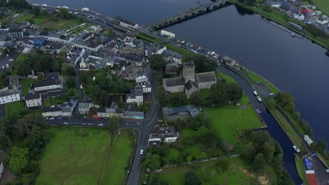 St Flannan's Cathedral, Killaloe, County Clare, Ireland, September 2021. Drone high angle aerial pullback tilts up to reveal the town and River Shannon on a wet gloomy overcast day.