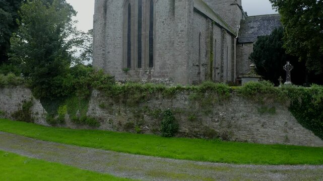 St Flannan's Cathedral, Killaloe, County Clare, Ireland, September 2021. Drone ascends showcasing the medieval architectural facade with thin narrow windows and cemetery on an overcast day.