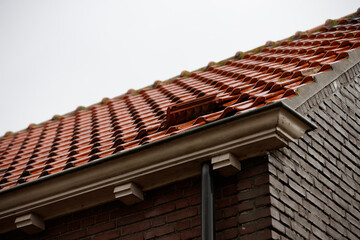 Close-up of a damaged section of a terracotta tile roof with exposed brick wall.  Repair needed.