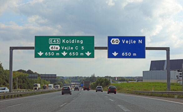 some road signs with directions to cities in Denmark in Northern Europe and cars driving by