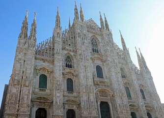 Wide facade of the Milan Cathedral in Gothic style with tall spires