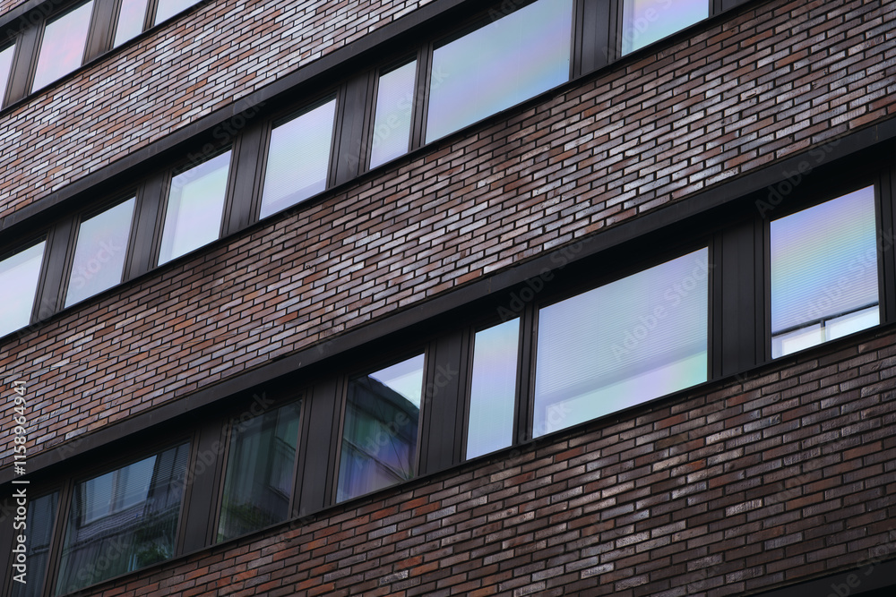 Poster a brick building with many windows. the windows are clear and reflect the sky. the building is tall 