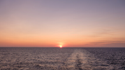 sunrise sun is setting over the ocean as beautiful backdrop for web page banner template. sky is beautiful mix of pink and purple.  water is calm and still, with a cruise ship's wake off  stern.