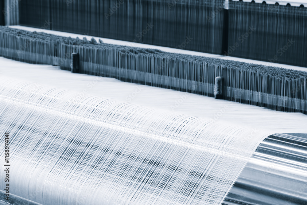 Leinwandbilder Machine is weaving a piece of fabric. The machine is made of metal and has a silver color. The fabric is white and has a striped pattern. The machine is in motion