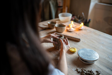 Potter hands shape patterned clay cup on wooden table in workshop. Craftsmanship, ceramic design, pottery class, handmade crockery, creative occupation, craft and master class, do it yourself