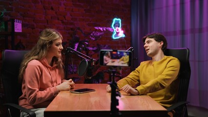 Man host and woman guest recording interview in loft podcast studio using microphones and...