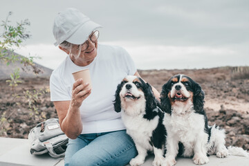 Senior smiling woman sitting outdoors with her two cavalier king charles spaniel dogs enjoying...