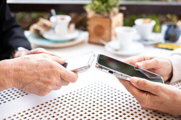 Close up view of two modern women's hands using apps and wireless technology to share files or photos between their smartphones
