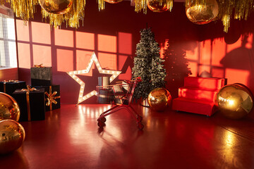 A gift cart in a red room with sunlight. New Year's decor. Christmas tree in the interior of the house in red and gold tones with space for copying. High quality photo