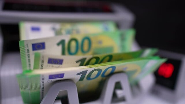 One hundred euro bills appear on the holder of machine. Money counted quickly by the bank equipment. Close up.