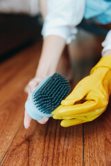 Person in yellow rubber gloves cleaning wooden floor with toothbrush