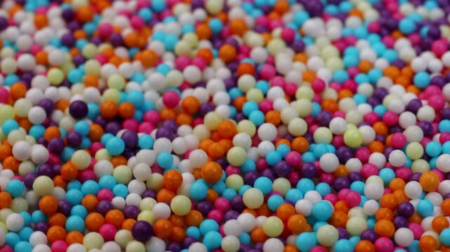 Texture of colored sprinkles small tiny beads, rotation in circle. Colorful sugar sprinkles, Turning. Sweet rainbow sprinkles, Multi colored candy decorations. 
