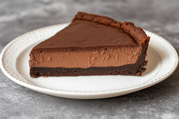 A decadent slice of chocolate tart featuring smooth layers of chocolate filling and crust, served on a white plate