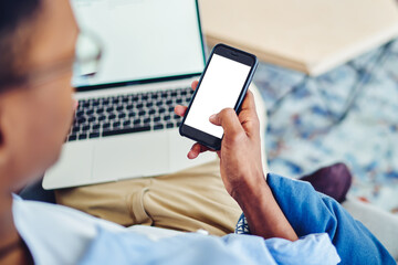 Crop black freelancer with laptop using smartphone