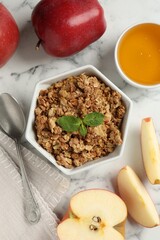 Tasty apple crisp in bowl, fresh fruits, honey and spoon on white marble table, flat lay