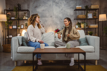 Obraz premium two young adult female friends sit on sofa and enjoy while chatting