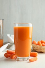 Fresh carrot juice in glass and vegetables on white table against gray background