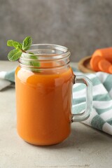 Fresh carrot juice and mint in mason jar on gray textured table
