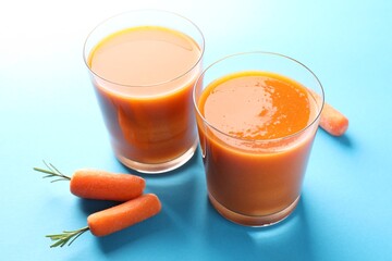 Fresh carrot smoothie in glasses and vegetables on light blue background, closeup