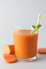 Fresh carrot smoothie in glass and cut vegetable on light grey background, closeup