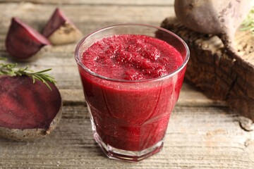 Fresh beetroot smoothie in glass, rosemary and cut vegetables on wooden table, closeup