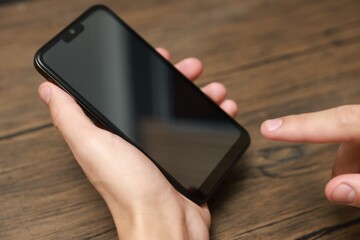 Man using smartphone with blank screen at wooden table, closeup