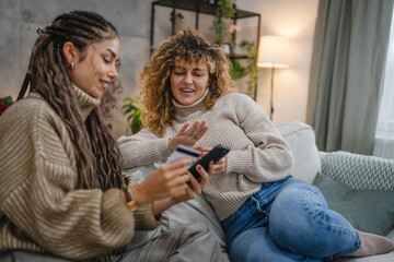 two friendly women use cellphone and credit card make payments online