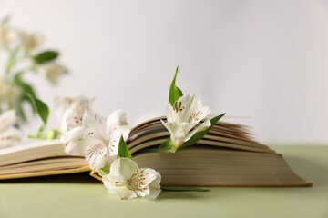 Book and beautiful alstroemeria flowers on green table against light background, closeup