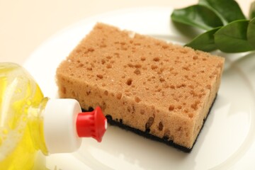 Sponge, detergent and plate on beige background, closeup