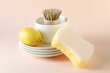 Sponge, dishware, lemon and brush on beige background, closeup