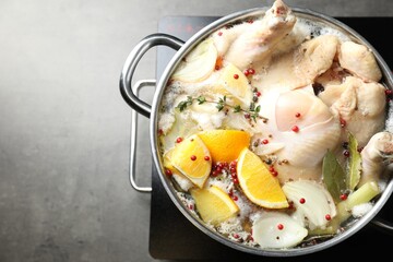 Whole fresh turkey, cut citrus fruits, thyme and spices boiling in pot on stove on grey table, top view. Space for text