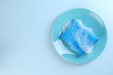 One sponge with foam and plate on light blue background, top view. Space for text