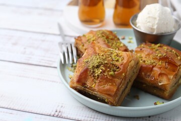 Delicious baklava with crushed nuts and ice cream on white wooden table, closeup. Space for text