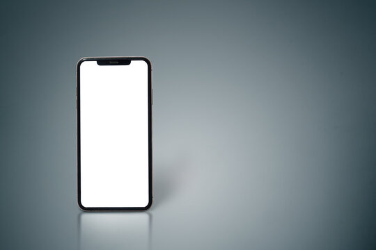 A white phone is sitting on a grey surface. The screen is black and the phone is turned off