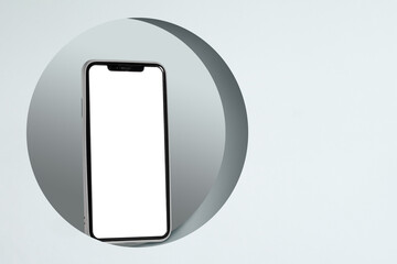 A white phone is placed inside a circular frame, which is also white. The frame is centered in the picture, and the phone is placed on top.