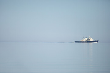 ship sails across a calm, endless sea under a pale blue sky