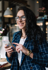 Satisfied female freelancer surfing cellphone in cafeteria