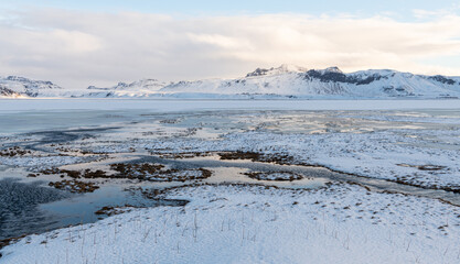 View on frozen sea and snowy volcanic mountains in the background, Iceland. Near Reynisfjara beach and reynisdrangar sea stacks, south coast of Iceland winter time. Ice and snow, remote location.