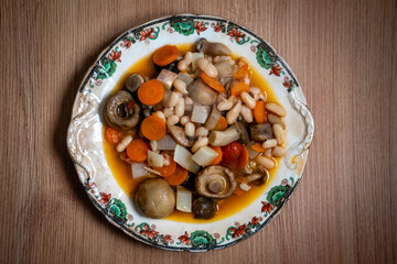 Mushroom and white bean stew served on a rustic wooden table in a traditional restaurant setting, showcasing warm, hearty comfort food in a cozy atmosphere.