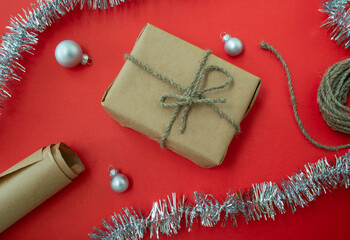 Packing Christmas gifts. Gift, twine and paper, Christmas balls and tinsel on a red background.