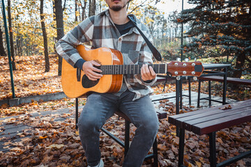 Guitarist, dressed in a cozy plaid shirt, strums an acoustic guitar while seated among autumn...
