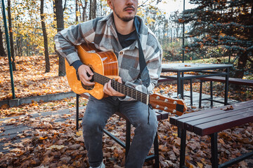 Guitarist, dressed in a cozy plaid shirt, strums an acoustic guitar while seated among autumn...