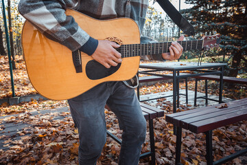 Guitarist, dressed in a cozy plaid shirt, strums an acoustic guitar while seated among autumn...