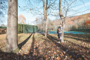 Musician plays an acoustic guitar in a sunlit park during autumn, surrounded by fallen leaves and natural beauty. The vibrant setting complements the musical performance